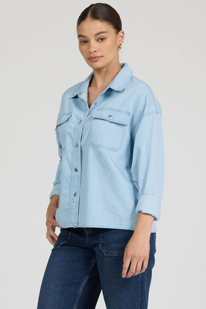 Woman wearing a light blue denim shirt and dark jeans on a plain background