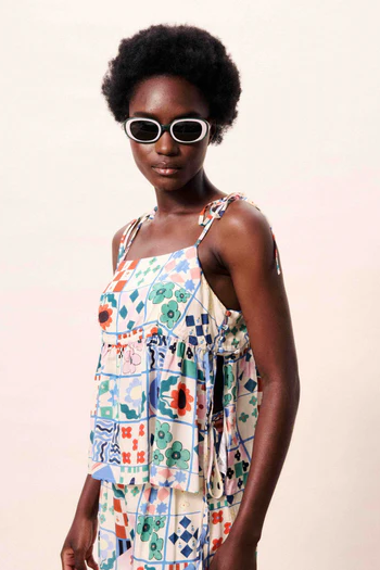 Woman wearing a colorful patterned dress and sunglasses against a plain background