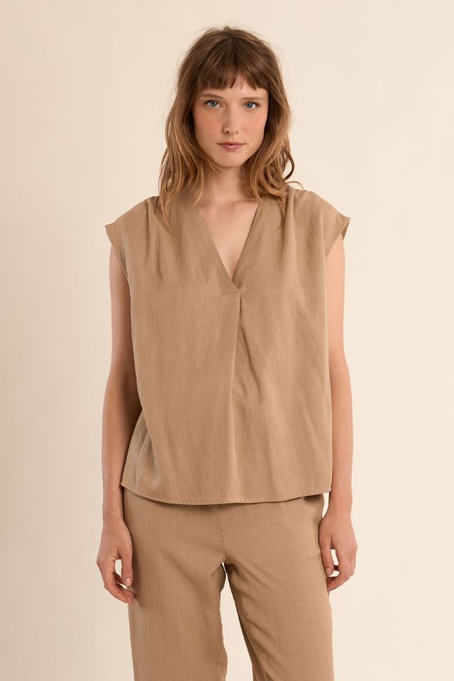 Woman wearing a beige sleeveless top and pants against a beige background