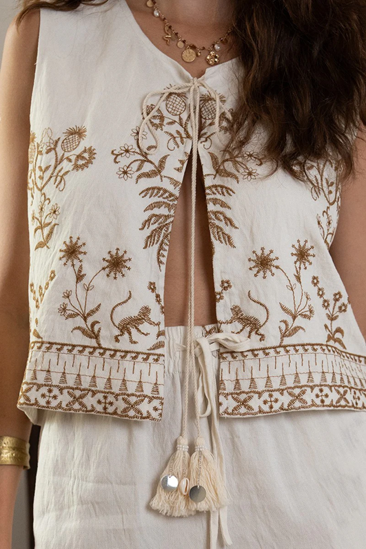 White sleeveless top with intricate gold embroidery on a person wearing it.