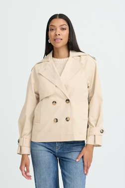 Woman wearing a beige trench coat and blue jeans on a white background