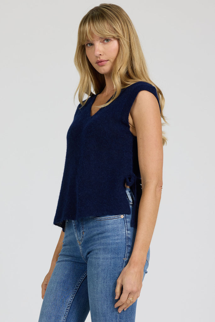 Woman wearing a navy sleeveless top and blue jeans on a plain background
