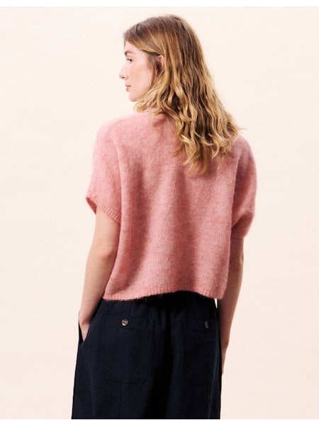Person wearing a pink sweater and black pants on a light pink background