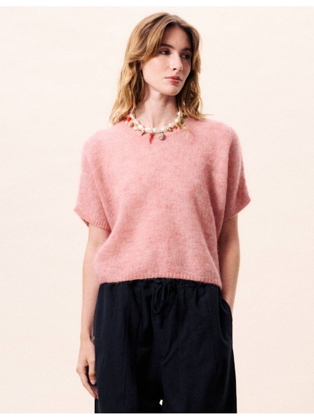 Woman wearing a pink sweater and black pants on a light pink background