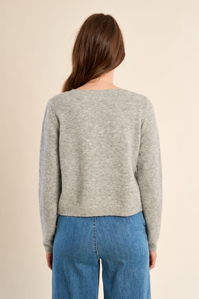 back of a girl wearing a grey cardigan and jeans against a white background