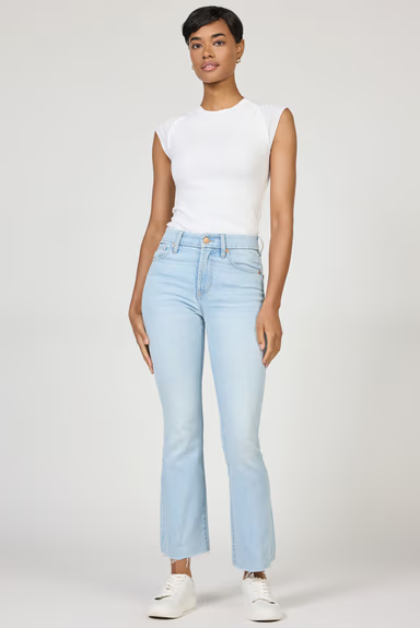 Woman wearing light blue jeans and a white top on a plain background