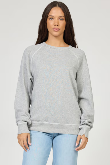 Woman wearing a gray sweatshirt and light blue jeans on a plain background