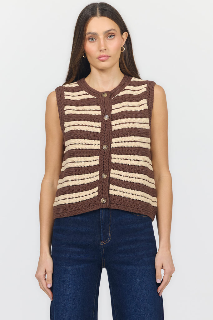 A woman modeling a sleeveless knit vest with horizontal brown, beige, and white stripes, paired with dark blue jeans against a plain white background.
