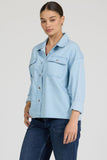 Woman wearing a light blue denim shirt and dark jeans on a plain background