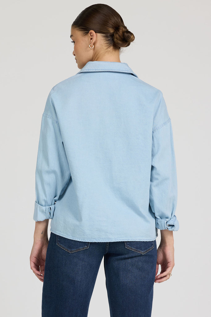 Woman wearing a light blue shirt and dark blue jeans on a plain background
