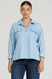 Woman wearing a light blue denim shirt and dark jeans on a plain background