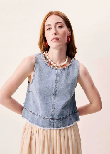 Woman wearing a denim top and beige skirt with a plain background