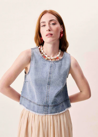 Woman wearing a denim top and beige skirt with a plain background