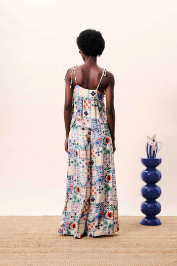 Woman wearing a floral dress standing in front of a blue vase on a wooden floor.