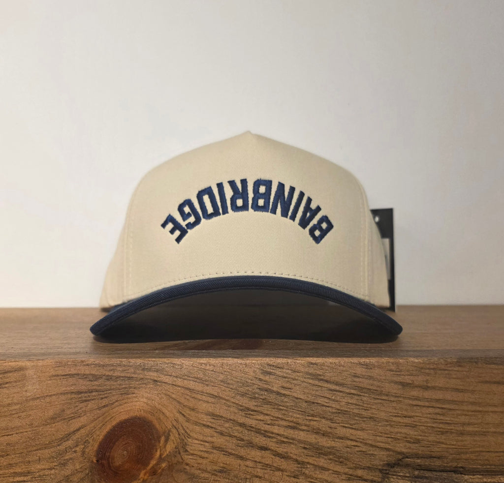Beige cap with 'Bainbridge' text on a wooden surface