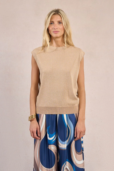 Woman wearing a beige sleeveless top and patterned pants on a plain background