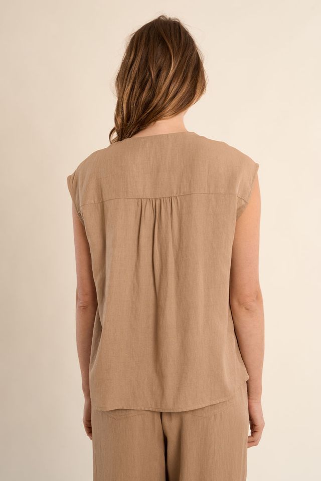 Woman wearing a beige sleeveless top and pants against a beige background