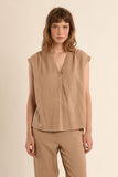 Woman wearing a beige sleeveless top and pants against a beige background