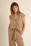 Woman wearing a beige sleeveless top and pants on a beige background
