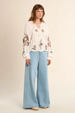 Woman wearing a floral blouse and light blue jeans on a beige background