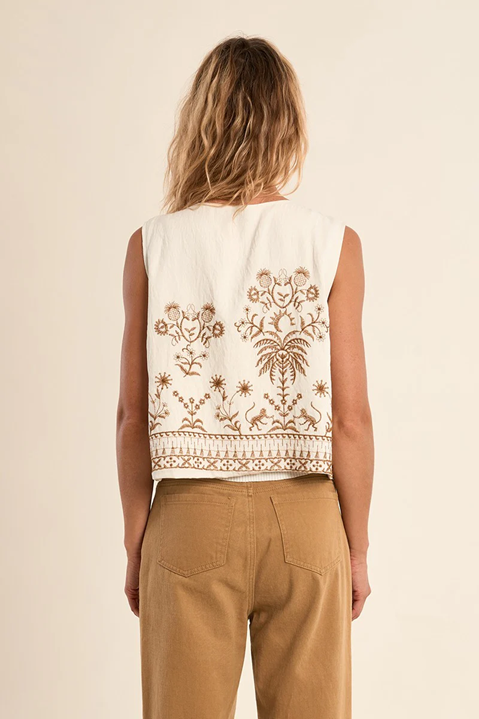 Woman wearing a sleeveless top with intricate brown embroidery on a beige background