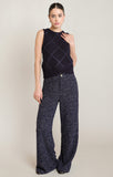 Woman wearing a dark patterned sleeveless top and wide-leg pants against a plain background