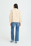 Person wearing a beige jacket and blue jeans on a white background