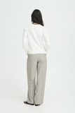 Person wearing a white sweater and light gray pants on a white background