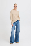 woman in beige sweater and flare jeans against white background