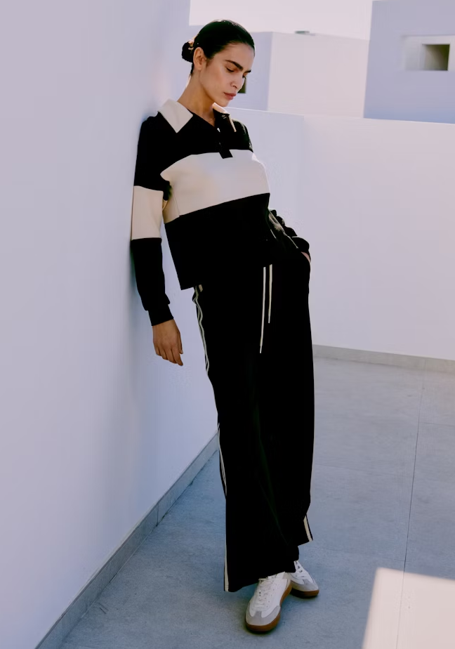 Person wearing a black and white striped sweater and black pants in a minimalistic room.