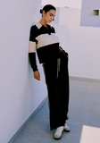 Person wearing a black and white striped sweater and black pants in a minimalistic room.