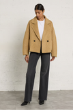 woman in camel coat and black pants against white background