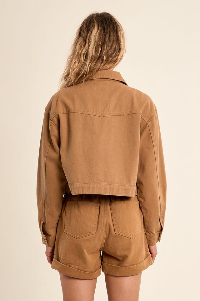 Person wearing a brown jacket and shorts set on a beige background