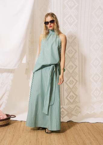 Woman wearing a green and white striped dress against a textured white curtain.