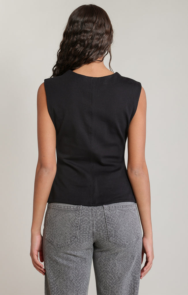 back of woman in black sleeveless shirt and jeans against white wall