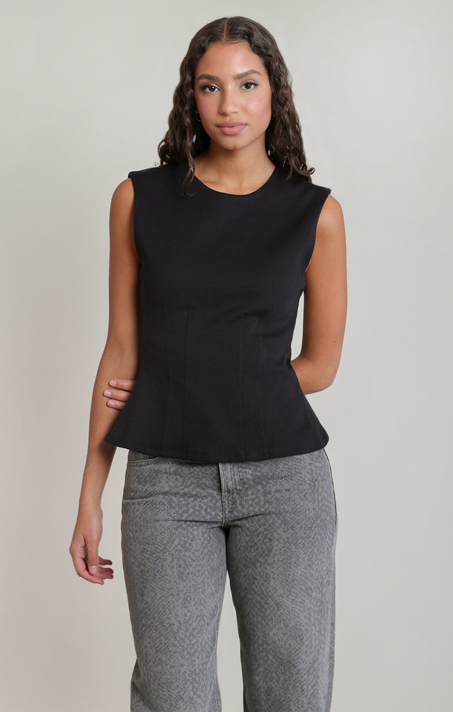 woman in black sleeveless shirt and jeans against white wall
