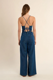 Woman wearing a blue denim jumpsuit with a backless design on a beige background