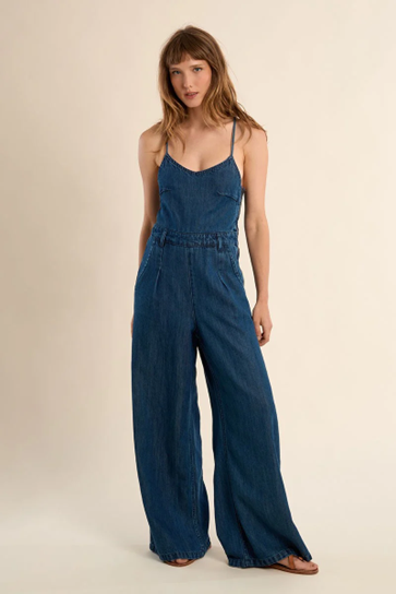 Woman wearing a blue denim jumpsuit on a beige background