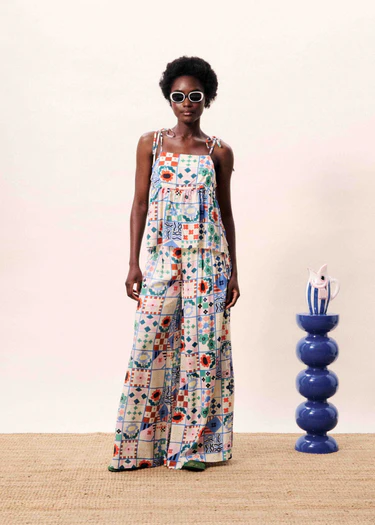 Woman wearing a colorful patterned dress standing next to a blue vase on a wooden floor.