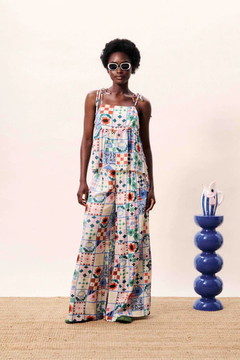 Woman wearing a colorful patterned dress standing next to a blue vase on a wooden floor.