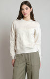 A woman modeling a cream-colored crewneck sweatshirt with tonal floral embroidery on the front and sleeves, paired with olive green cargo pants, against a neutral gray background.