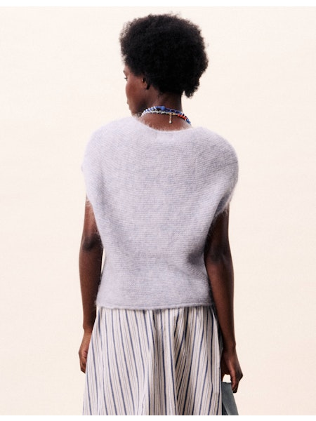 Person wearing a light gray sleeveless top and striped pants on a beige background