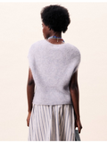 Person wearing a light gray sleeveless top and striped pants on a beige background