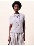 Woman wearing a light gray sleeveless sweater and striped pants against a white background