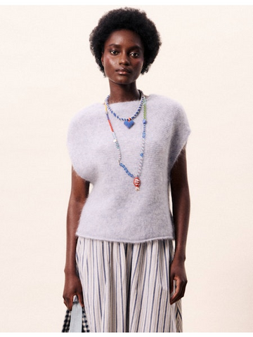 Woman wearing a light gray sleeveless sweater and striped pants against a white background