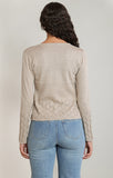 Person wearing a beige cable knit sweater and light blue jeans on a plain background