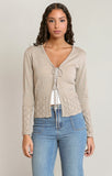 Woman wearing a beige cable knit cardigan and blue jeans on a plain background