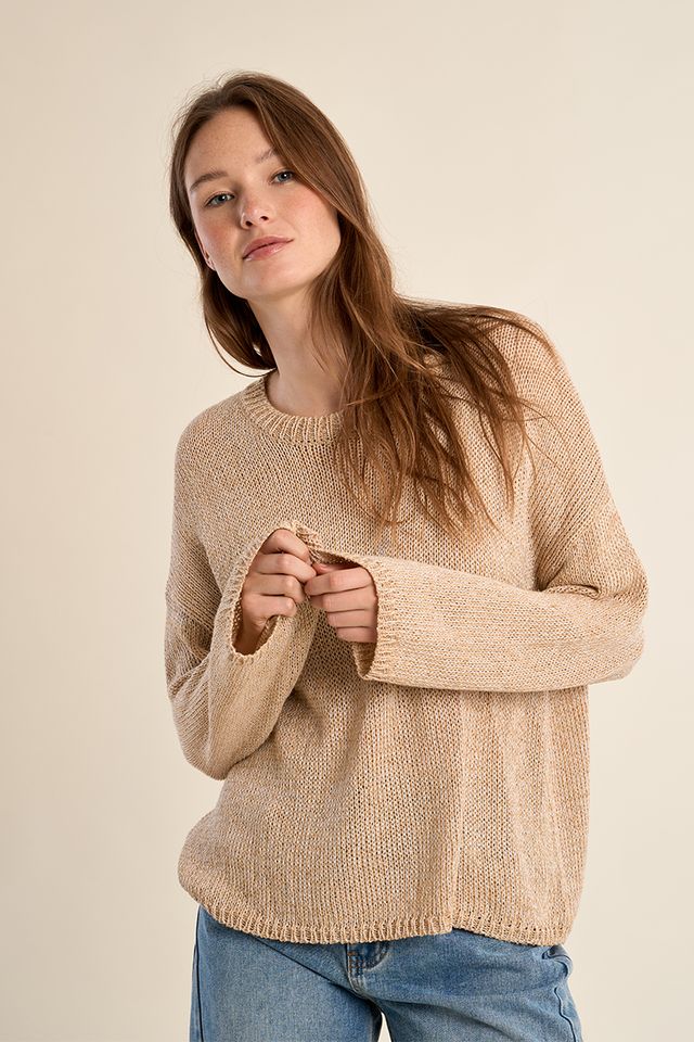 Woman wearing a beige sweater and blue jeans against a plain background
