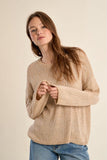 Woman wearing a beige sweater and blue jeans against a plain background