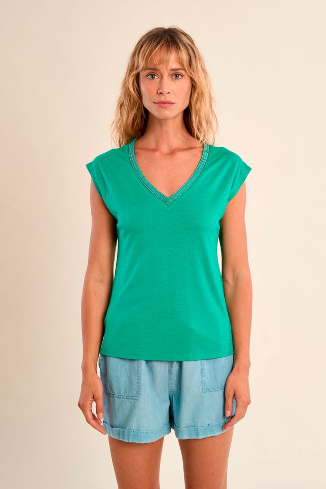 Woman wearing a green top and light blue shorts on a beige background